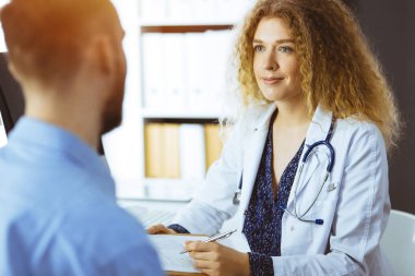 Kadın doktor ve erkek hasta güneşli klinikte otururken sağlık muayenesini tartışıyorlar. Tıp konsepti