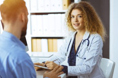 Kadın doktor ve erkek hasta güneşli klinikte otururken sağlık muayenesini tartışıyorlar. Tıp konsepti