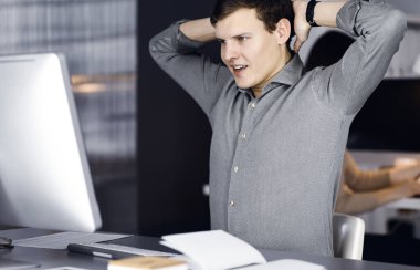 Yeşil tişörtlü kahverengi kıvırcık saçlı genç işadamı ve programcı, bilgisayar üzerinde sıkı çalıştıktan sonra ellerini uzatıyor ve kadın meslektaşıyla birlikte kabinede oturuyor. İş dünyası