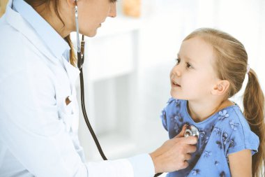 Doktor steteskopla küçük bir kızı muayene ediyor. Her zamanki tıbbi muayenede gülümseyen çocuk hasta. Tıp ve sağlık hizmetleri kavramları