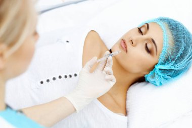 Profesyonel kozmetik uzmanı yüzüne ve dudaklarına iğne yapıyor. Genç bir kadın, yüz hatları ya da büyütme için doldurucu iğneyle doldurulur. Yaşlanma, gençleşme ve hidrasyon prosedürleriyle yüzleş