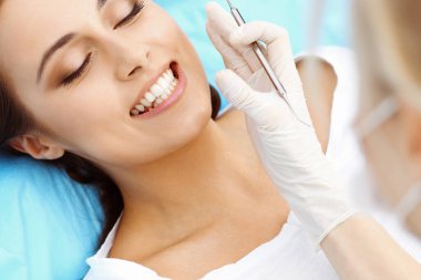 Genç bayan hasta dişçi muayenehanesini ziyaret ediyor. Sağlıklı, beyaz dişleri olan güzel bir kadın diş hekimliğinde çalışırken ağız muayenesi sırasında diş sandalyesinde oturuyor.