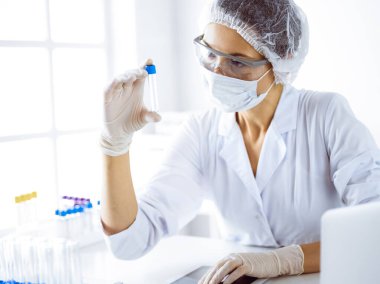 Koruyucu gözlüklü profesyonel kadın bilim adamı laboratuarda reaktörlerle araştırma tüpü kullanıyor. Tıp ve bilim araştırmaları kavramları