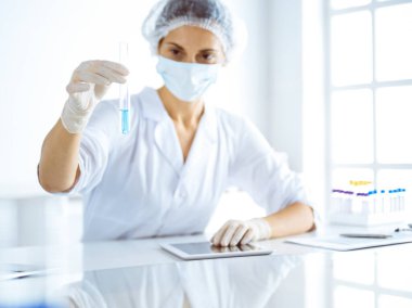 Koruyucu gözlüklü profesyonel kadın bilim adamı laboratuarda reaktörlerle araştırma tüpü kullanıyor. Tıp ve bilim araştırmaları kavramları