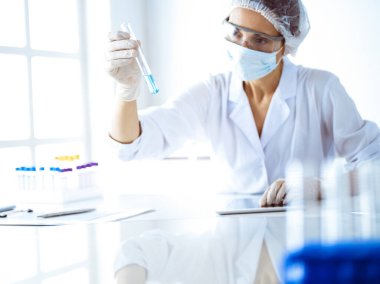 Koruyucu gözlüklü profesyonel kadın bilim adamı laboratuarda reaktörlerle araştırma tüpü kullanıyor. Tıp ve bilim araştırmaları kavramları