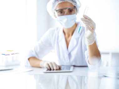 Koruyucu gözlüklü profesyonel kadın bilim adamı laboratuarda reaktörlerle araştırma tüpü kullanıyor. Tıp ve bilim araştırmaları kavramları