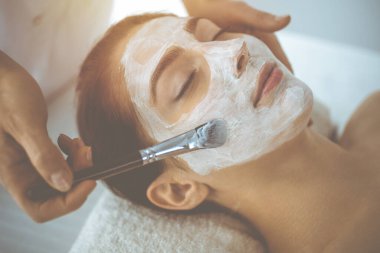 Güzel esmer kadın kapalı gözlerle kozmetik maske takmaktan zevk alıyor. Tıp ve kaplıca kavramlarında rahatlatıcı tedavi