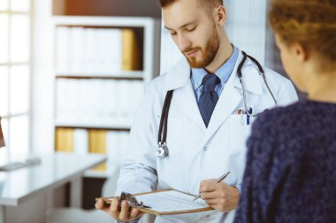 Dost canlısı kızıl sakallı doktor ve hasta kadın güneşli klinikte otururken sağlık muayenesini tartışıyorlar. Tıp konsepti