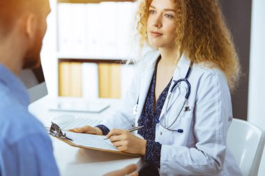 Kadın doktor ve erkek hasta güneşli klinikte otururken sağlık muayenesini tartışıyorlar. Tıp konsepti