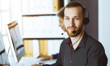 Günümüz güneşli ofisinde otururken, kulaklıkla konuşan kızıl sakallı bir iş adamı. Çağrı merkezinde çeşitli insanlar grubu