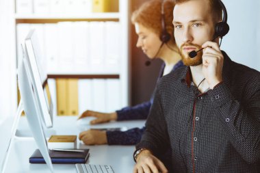 Günümüz güneşli ofisinde otururken, kulaklıkla konuşan kızıl sakallı bir iş adamı. Çağrı merkezinde çeşitli insanlar grubu