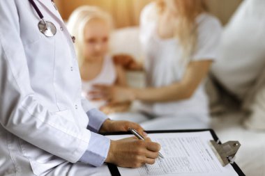 Doktor ve hasta. Pediyatrist, annesiyle birlikte küçük kızı muayene ederken pano kullanıyor. Sağlık muayenesinde hasta ve mutsuz bir çocuk.