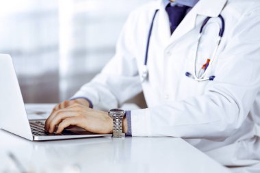 Bilinmeyen bir erkek doktor klinikte dizüstü bilgisayarla yakın planda çalışıyor. İşteki genç doktor. Mükemmel sağlık hizmeti, tıp konsepti