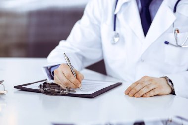 Bilinmeyen erkek doktor, klinikteki ilaç geçmişi kayıtlarıyla birlikte yakın planda oturuyor. İşteki genç doktor. Mükemmel sağlık hizmeti, tıp konsepti