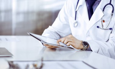 Bilinmeyen erkek doktor klinikteki tablet bilgisayarla yakın planda çalışıyor. İşteki genç doktor. Mükemmel sağlık hizmeti, tıp konsepti