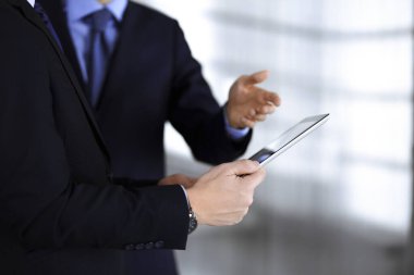 İş adamları yeni projelerini tartışmak için bir tablet bilgisayar kullanıyorlar, modern bir ofiste duruyorlar. İş yerinde iş arkadaşı olan tanınmamış bir iş adamı ya da erkek girişimci. Takım çalışması ve ortaklık