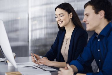 Çalışma masasında birlikte otururken iş yerindeki genç ve dost canlısı iş adamları. Kadınlara odaklan. Modern bir ofiste vesikalık ya da iş portresi