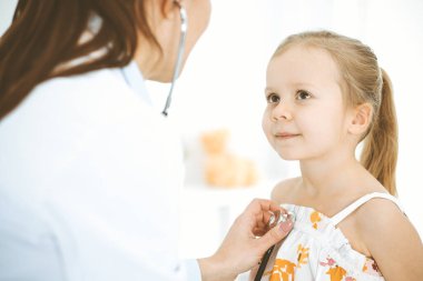 Doktor steteskopla küçük bir kızı muayene ediyor. Her zamanki tıbbi muayenede gülümseyen çocuk hasta. Tıp ve sağlık hizmetleri kavramları