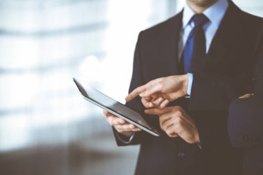 İş adamları yeni projelerini tartışmak için bir tablet bilgisayar kullanıyorlar, modern bir ofiste duruyorlar. İş yerinde iş arkadaşı olan tanınmamış bir iş adamı ya da erkek girişimci. Takım çalışması ve ortaklık