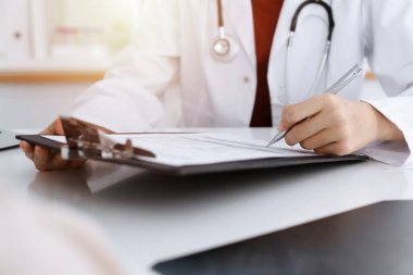 Bilinmeyen kadın-doktor hastaya danışmanlık yaparken başvuru formu dolduruyor. güneşli oda tıp konseptinde