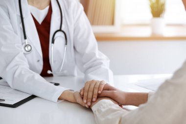 Kimliği belirsiz kadın doktorun elleri güneşli odada kadın hastasına güvence veriyor.