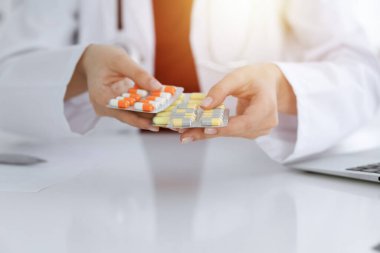 Bilinmeyen kadın doktor güneşli odada farklı tablet kabarcıkları sunuyor, yakın plan.