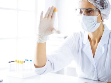 Koruyucu gözlüklü profesyonel kadın bilim adamı laboratuarda reaktörlerle araştırma tüpü kullanıyor. Tıp ve bilim araştırmaları kavramları