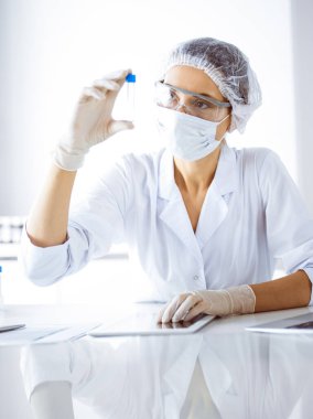 Koruyucu gözlüklü profesyonel kadın bilim adamı laboratuarda reaktörlerle araştırma tüpü kullanıyor. Tıp ve bilim araştırmaları kavramları