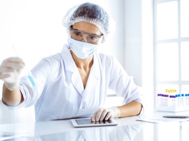 Koruyucu gözlüklü profesyonel kadın bilim adamı laboratuarda reaktörlerle araştırma tüpü kullanıyor. Tıp ve bilim araştırmaları kavramları