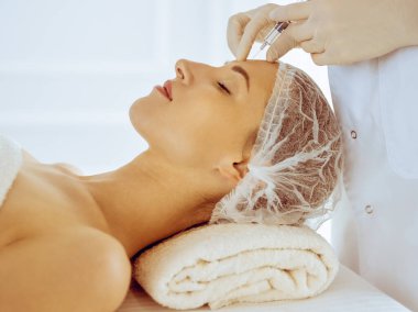 Güzel bir kadın tıp merkezinde kapalı gözlerle güzellik iğneleri yaptırıyor. Güzellik uzmanı elleri şırıngayla kadın yüzüne güzellik prosedürü uyguluyor.