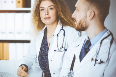 Güneşli klinikte arka planda erkek arkadaşıyla klinikte oturan arkadaş canlısı bayan doktor. Tıp konsepti