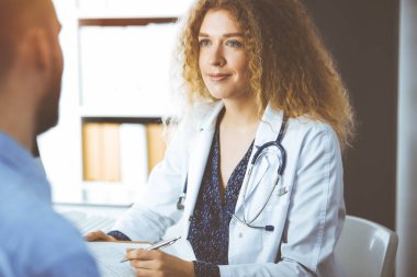 Kadın doktor ve erkek hasta güneşli klinikte otururken mevcut sağlık muayenesini tartışıyorlar.