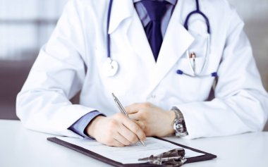 Bilinmeyen erkek doktor, klinikte, yakın planda pano ile oturuyor ve çalışıyor. İşteki genç doktor. Mükemmel sağlık hizmeti, tıp konsepti