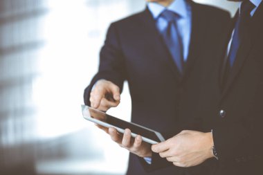 İş adamları yeni projelerini tartışmak için bir tablet bilgisayar kullanıyorlar, modern bir ofiste duruyorlar. İş yerinde iş arkadaşı olan tanınmamış bir iş adamı ya da erkek girişimci. Takım çalışması ve ortaklık