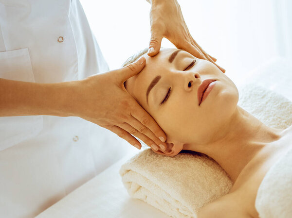 Beautiful woman enjoying facial massage with closed eyes in spa center. Relax treatment concept in medicine