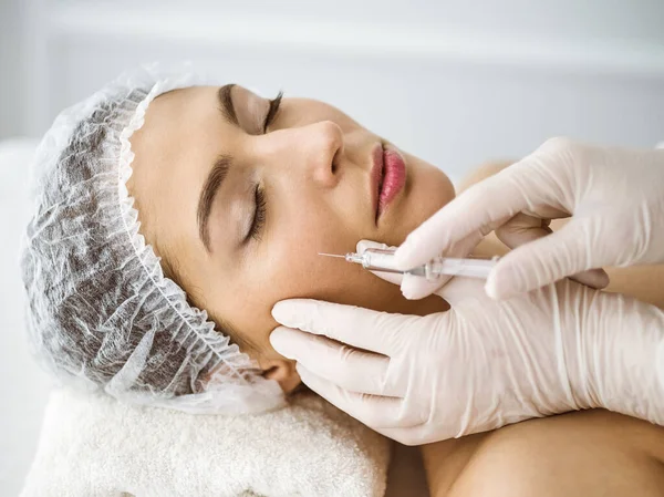 Güzellik uzmanı güneşli klinikte genç esmer kadının yüzüne şırıngayla güzellik prosedürü uyguluyor. Kozmetik ilaç ve ameliyat, güzellik iğneleri.