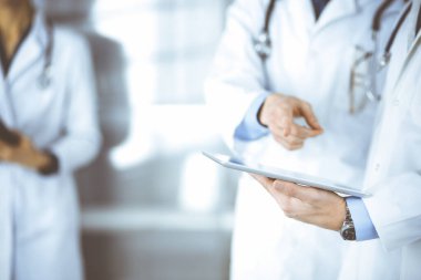 Bilinmeyen bir grup doktor hastane ofisinde dururken bazı tıbbi isim kayıtlarını kontrol etmek için bir bilgisayar tableti kullanıyor. Doktorlar hastaları muayene etmeye ve yardım etmeye hazır. Tıbbi yardım, sigorta