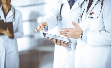 Bilinmeyen bir grup doktor hastane ofisinde dururken bazı tıbbi isim kayıtlarını kontrol etmek için bir bilgisayar tableti kullanıyor. Doktorlar hastaları muayene etmeye ve yardım etmeye hazır. Tıbbi yardım, sigorta