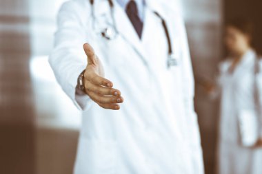 Bilinmeyen bir adam-doktor ayakta duruyor ve modern klinikte yardım eli uzatıyor. Kadın meslektaşının doktor geçmişinde acelesi var. Tıp konsepti