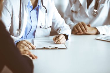 Bilinmeyen kadın-doktor ve erkek meslektaşı modern klinikte masa başında otururken hasta kadına danışıyorlar. Mükemmel bir tıbbi hizmet, Coronavirus salgını sırasında ilaç. Covid 2019