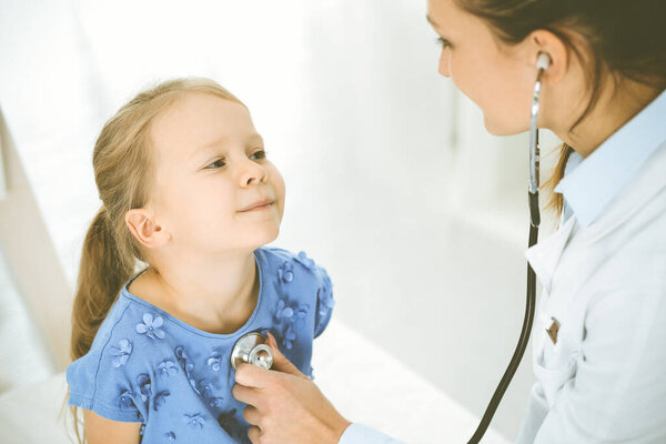 Врач осматривает ребенка стетоскопом. Счастливая улыбающаяся пациентка в синем платье при обычном медицинском осмотре. Концепция медицины