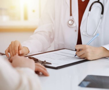 Bilinmeyen kadın-doktor hastaya danışmanlık yaparken başvuru formu dolduruyor. güneşli oda tıp konseptinde
