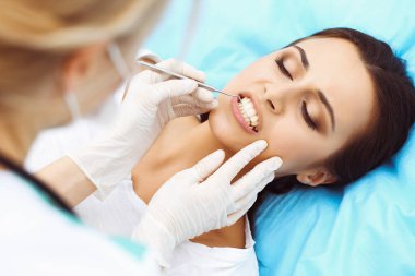 Genç bayan hasta dişçi muayenehanesini ziyaret ediyor. Sağlıklı, beyaz dişleri olan güzel bir kadın diş hekimliğinde çalışırken ağız muayenesi sırasında diş sandalyesinde oturuyor.