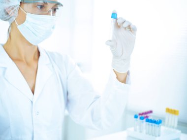 Koruyucu gözlüklü profesyonel kadın bilim adamı labaratuvarda mavi renkte reaksiyonlarla araştırma tüpü kullanıyor. Tıp ve bilim araştırmaları kavramları