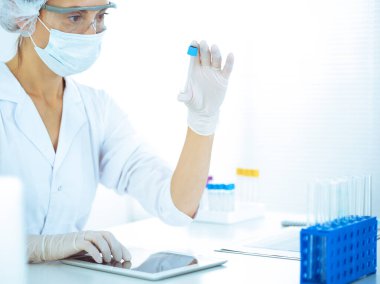 Koruyucu gözlüklü profesyonel kadın bilim adamı labaratuvarda mavi renkte reaksiyonlarla araştırma tüpü kullanıyor. Tıp ve bilim araştırmaları kavramları