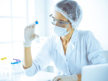 Koruyucu gözlüklü profesyonel kadın bilim adamı labaratuvarda mavi renkte reaksiyonlarla araştırma tüpü kullanıyor. Tıp ve bilim araştırmaları kavramları