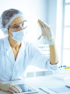 Koruyucu gözlüklü profesyonel kadın bilim adamı labaratuvarda mavi renkte reaksiyonlarla araştırma tüpü kullanıyor. Tıp ve bilim araştırmaları kavramları