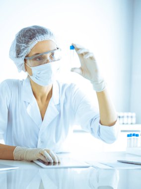 Koruyucu gözlüklü profesyonel kadın bilim adamı labaratuvarda mavi renkte reaksiyonlarla araştırma tüpü kullanıyor. Tıp ve bilim araştırmaları kavramları