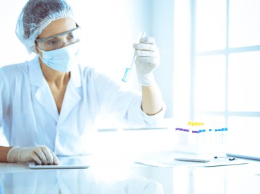 Koruyucu gözlüklü profesyonel kadın bilim adamı labaratuvarda mavi renkte reaksiyonlarla araştırma tüpü kullanıyor. Tıp ve bilim araştırmaları kavramları