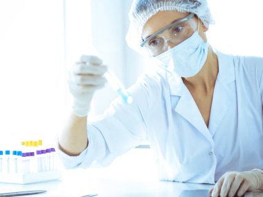 Koruyucu gözlüklü profesyonel kadın bilim adamı laboratuarda reaktörlerle araştırma tüpü kullanıyor. Tıp ve araştırma kavramları